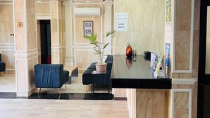 Een hotel lobby met een receptiebalie, een zithoek en een ingelijst beeld aan de muur.