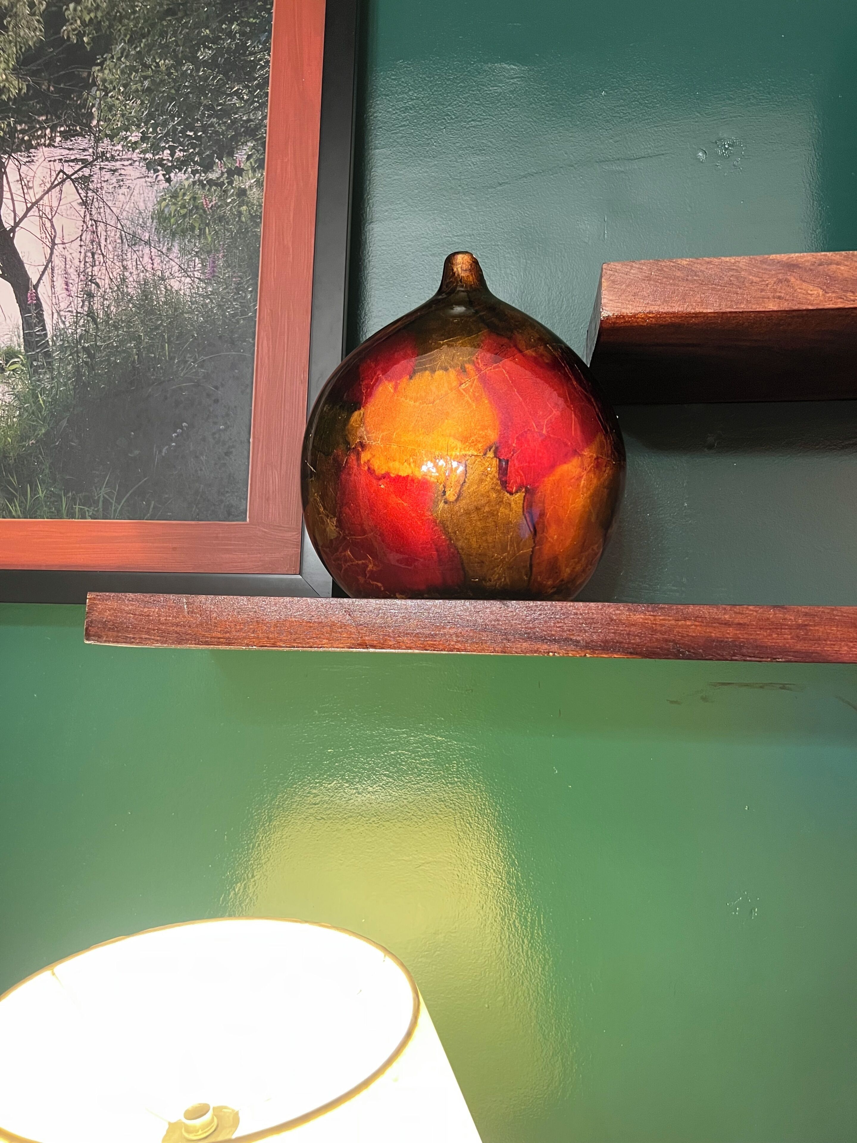 A pomegranate on a wooden shelf against a green wall.