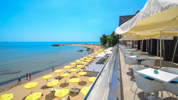 Een terras aan het strand met gele parasols en witte stoelen, met uitzicht op zee.
