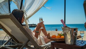 Iemand ontspant in een strandstoel met een drankje, een emmer vol fruit en een fles champagne.