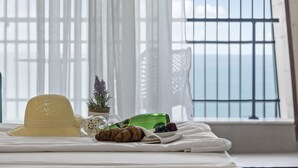 Een bed met een strohoed, croissant, een glas sap, een kleine potplant en een groene fles op een witte spreidekker.
