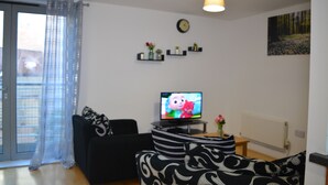 A living room with a black sofa, a television, a clock, and a painting on the wall. - Executive Apartment Cardiff Central (Cardiff)