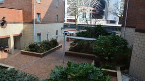 A courtyard with brick pathways, planters with greenery, and a modern building with a glass facade in the background. - Executive Apartment Cardiff Central (Cardiff)