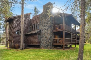 A rustic cabin with a stone chimney, wooden deck, and multiple windows.
