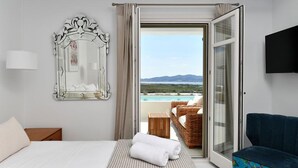 Un dormitorio con cama, un espejo grande, vista a una piscina y montañas, un sofá azul y un televisor en la pared.