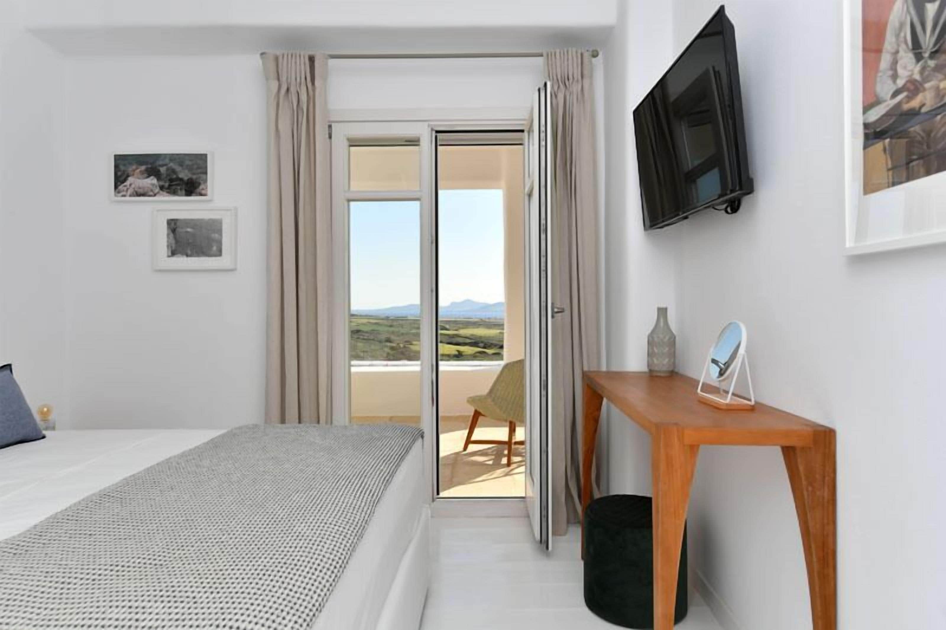 A bedroom with a bed, a desk, a chair, a TV, and a view of the outdoors.