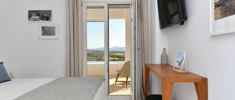 A bedroom with a bed, a desk, a chair, a TV, and a view of the outdoors.