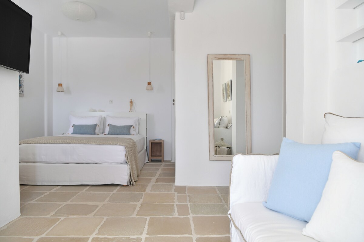A bedroom with a bed, a bedside table, a mirror, and a TV mounted on the wall.