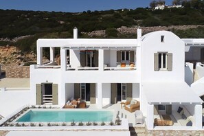 Un edificio blanco de dos pisos con piscina, asientos al aire libre y vistas a la colina.
