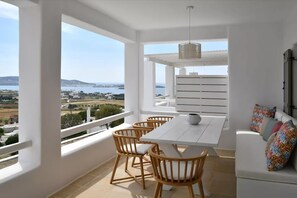 Un balcón con una mesa y sillas blancas, una lámpara colgante y un sofá blanco con cojines de colores.
