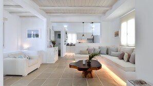 Un amplio salón con un sofá blanco, una mesa de centro de madera y una cocina al fondo.