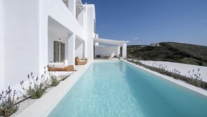 Un edificio moderno blanco con piscina, mobiliario exterior y vistas a un paisaje montañoso.