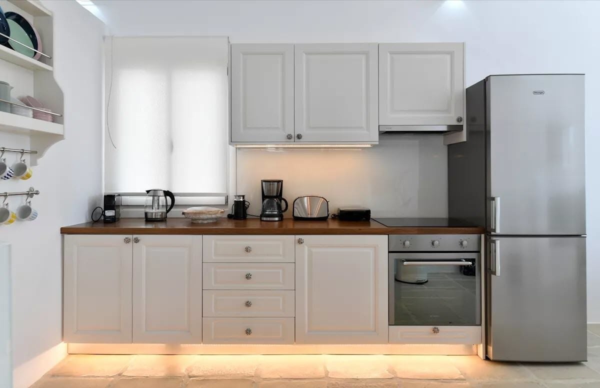 Een moderne keuken met witte kasten, een roestvrijstalen koelkast, een oven en een koffiezetapparaat.
