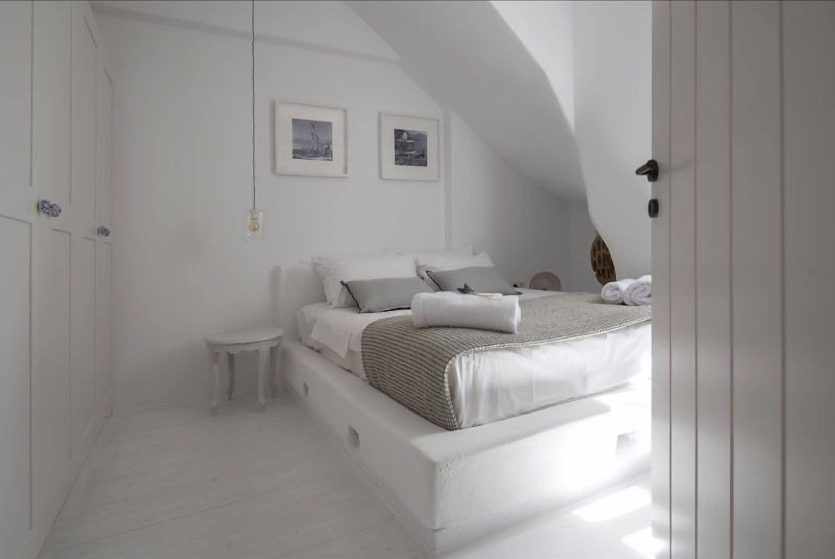 A bedroom with a white bed, a small bedside table, and two framed pictures on the wall.