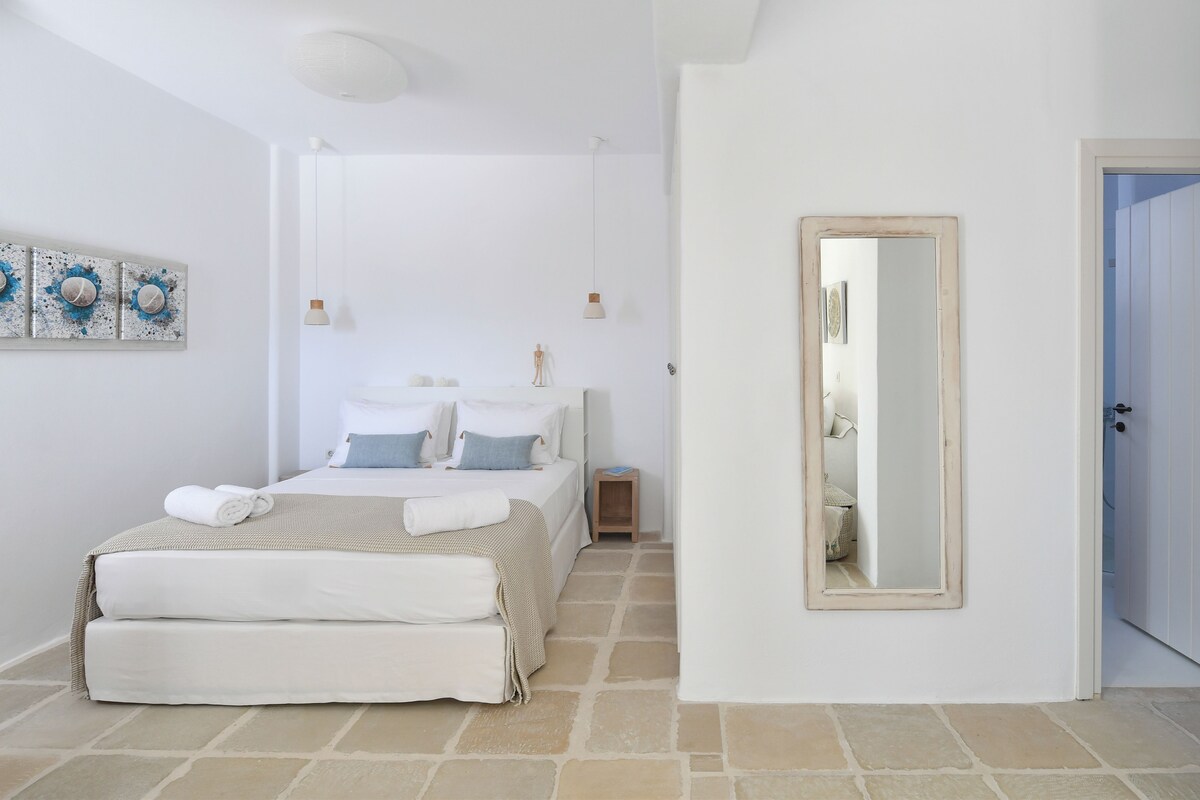 Un dormitorio con cama, mesitas de noche, un espejo y obras de arte en la pared.