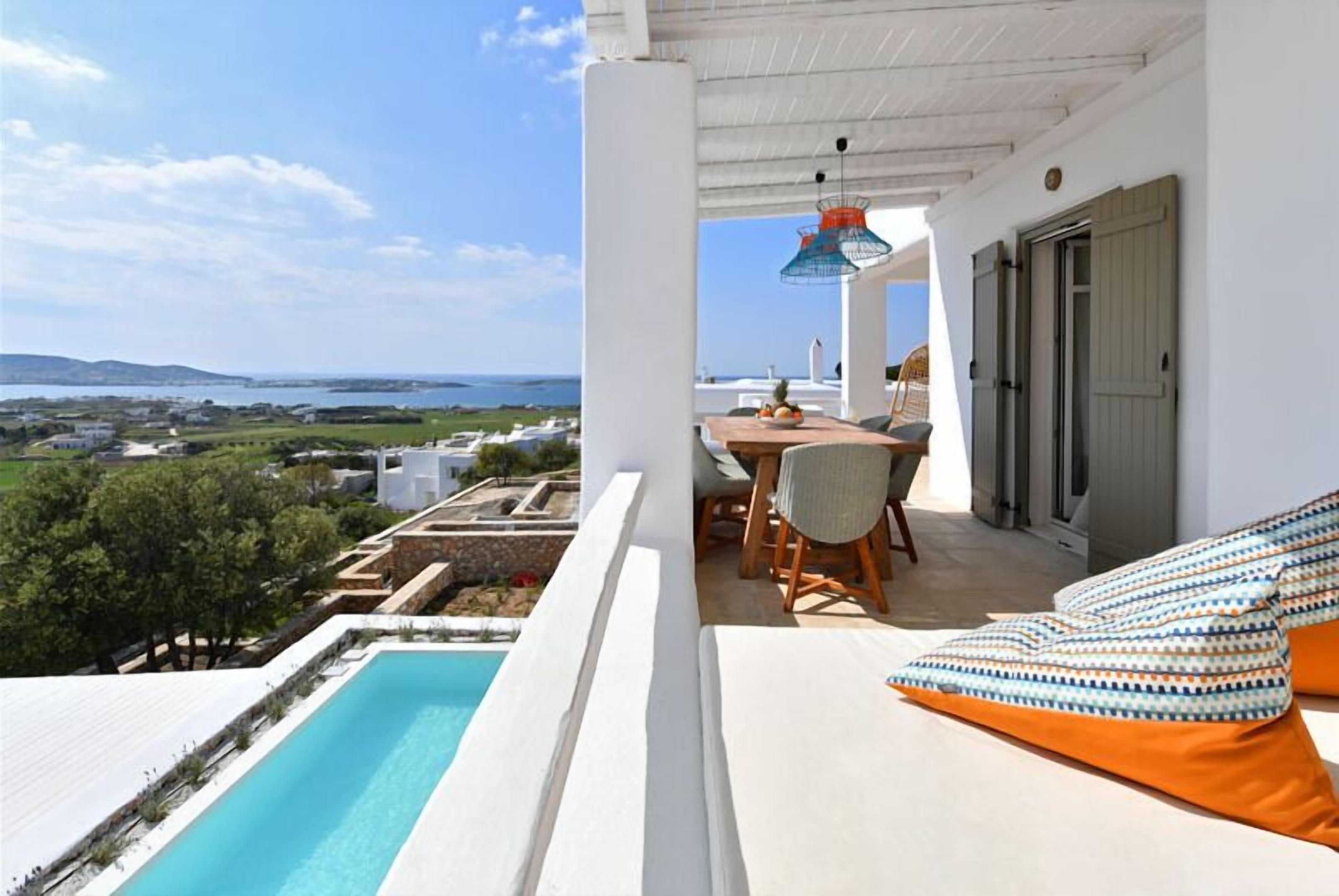 A balcony with a pool, a table with chairs, and a sofa with cushions.