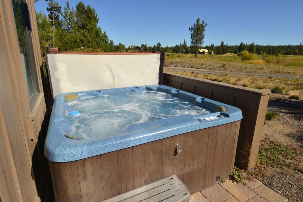 A wooden hot tub with a blue interior, set outdoors with a view of a natural landscape.