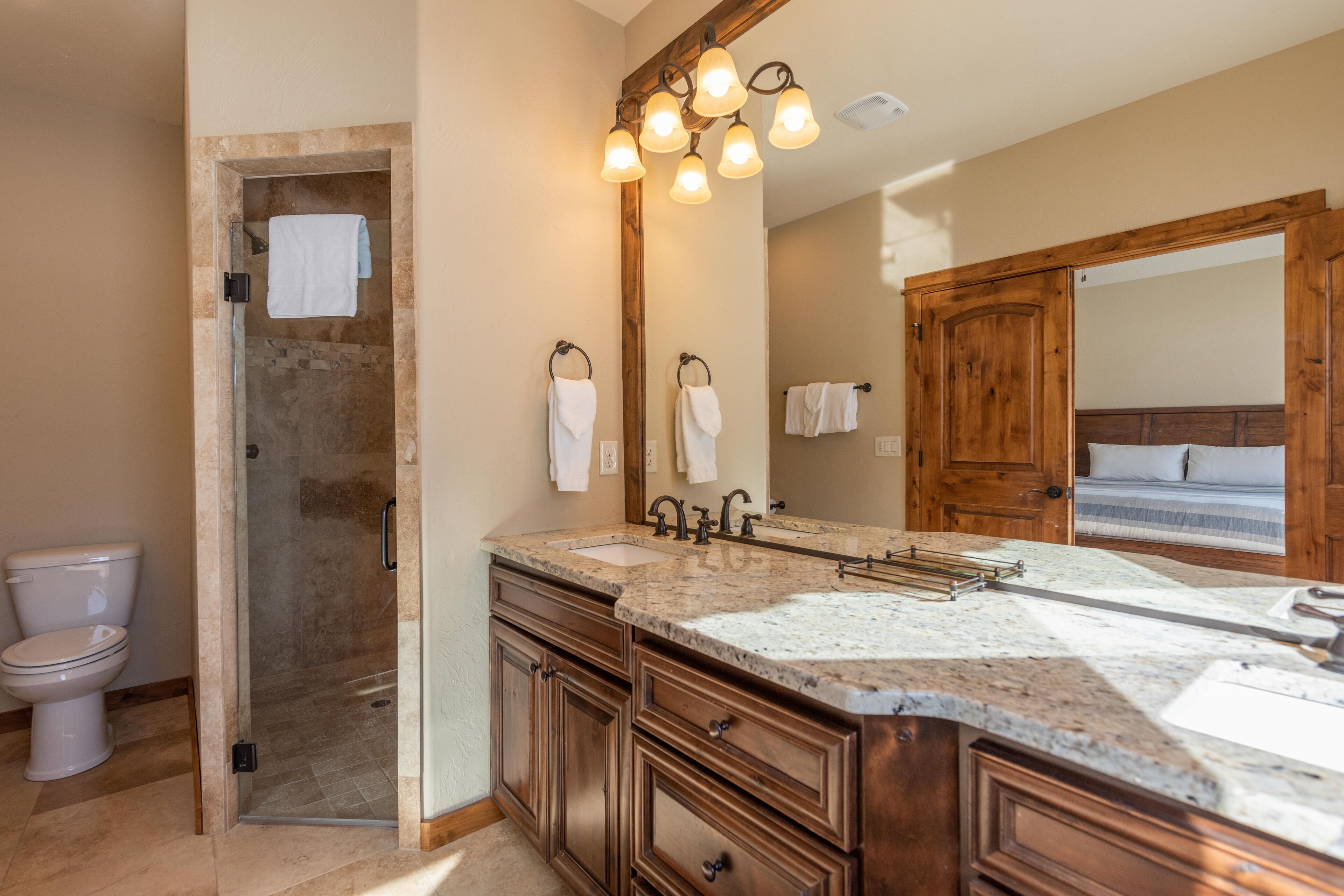 A bathroom with a shower, a toilet, a sink, and a large mirror.