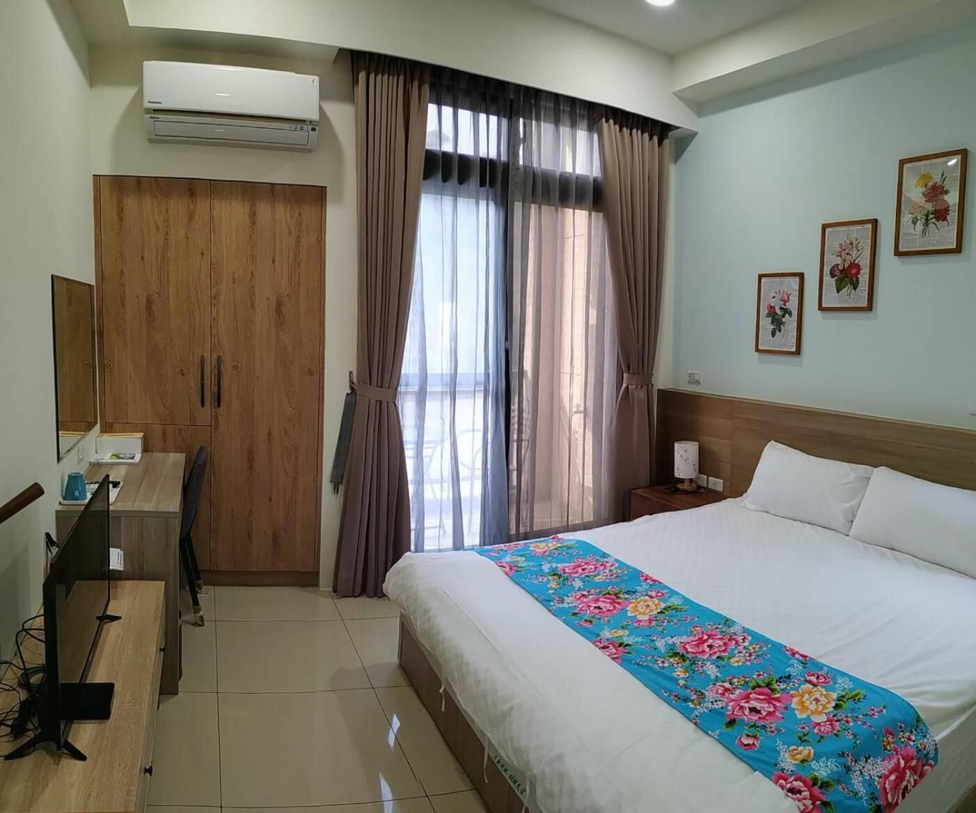 Una habitación de hotel con cama, escritorio, aire acondicionado, armario y cortinas.