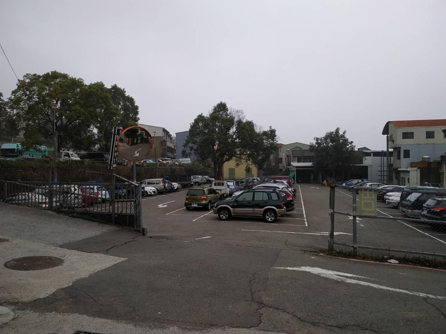 Un estacionamiento con varios coches y algunos edificios al fondo.