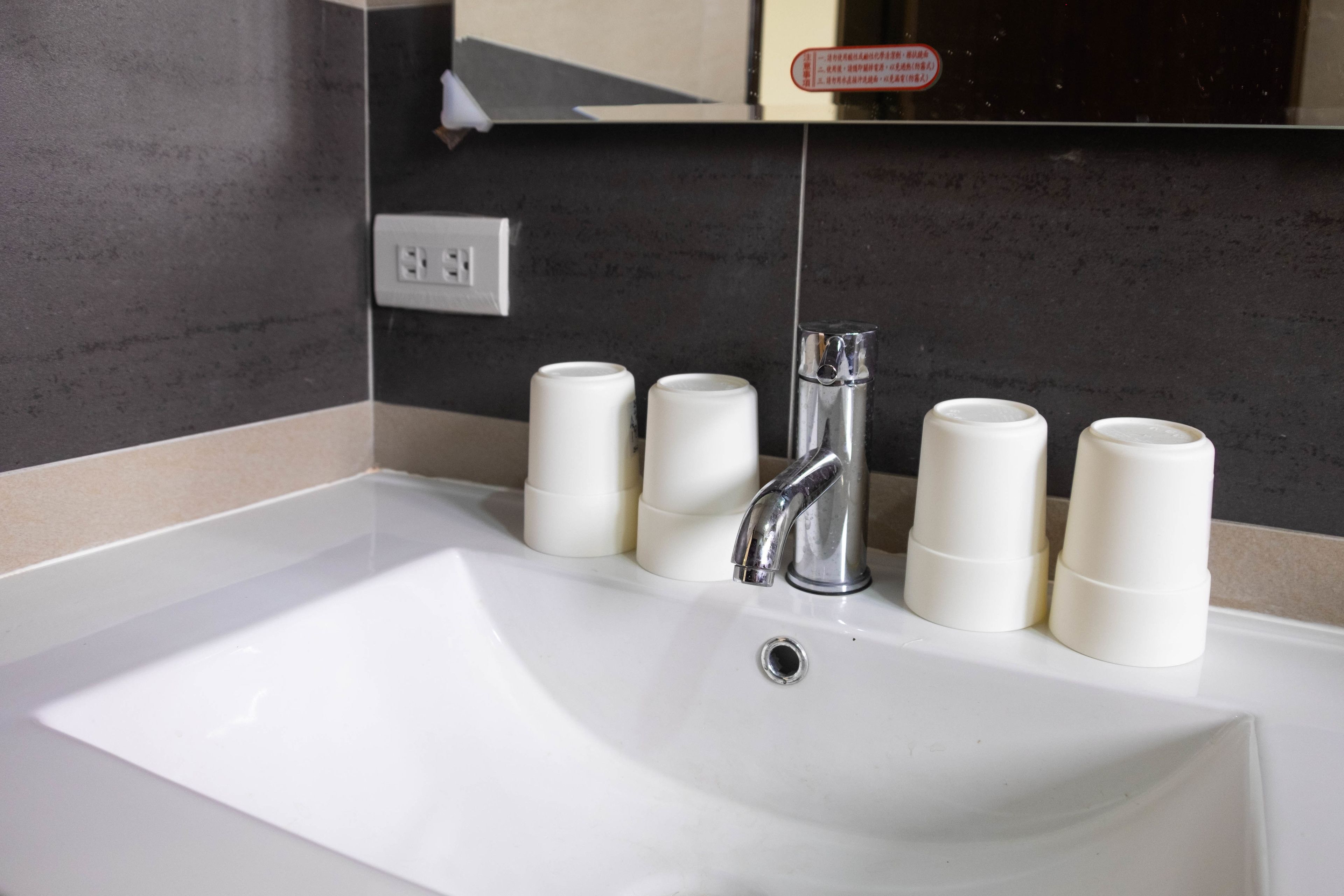 A white sink with a modern faucet, four white soap dispensers, and a mirror above.