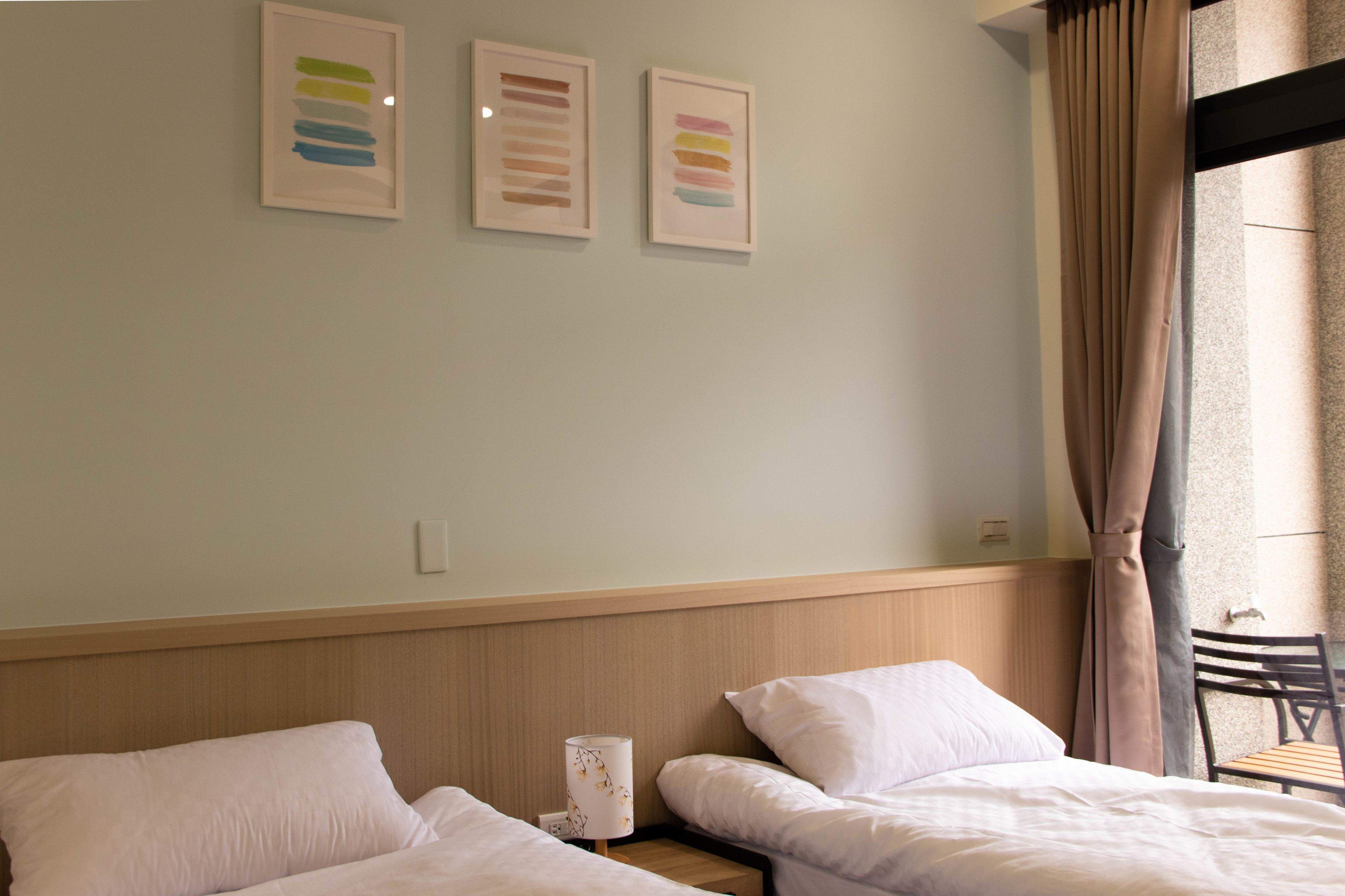 Habitación de hotel con dos camas, una mesita de noche con lámpara y tres cuadros enmarcados en la pared.