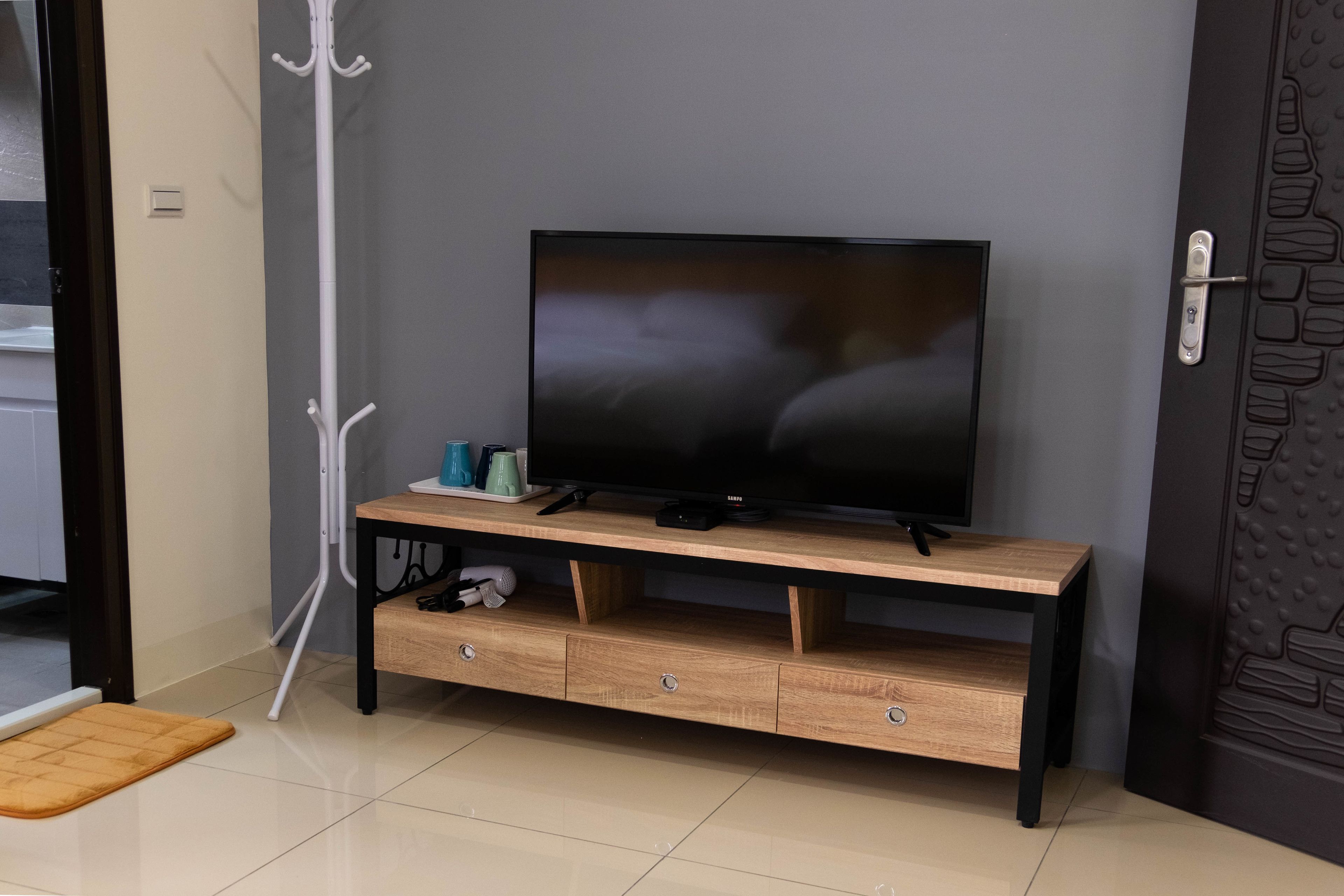 A TV on a wooden stand with a coat rack beside it.