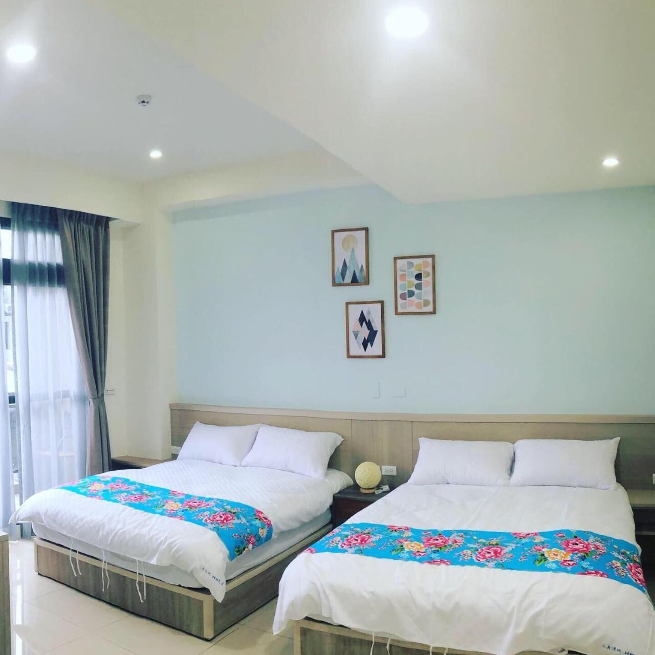 A hotel room with two beds, a large window with curtains, and wall art.