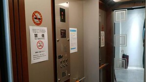 Een liftinterieur met een rookverbodsbord, noodinstructies en een bedieningspaneel.