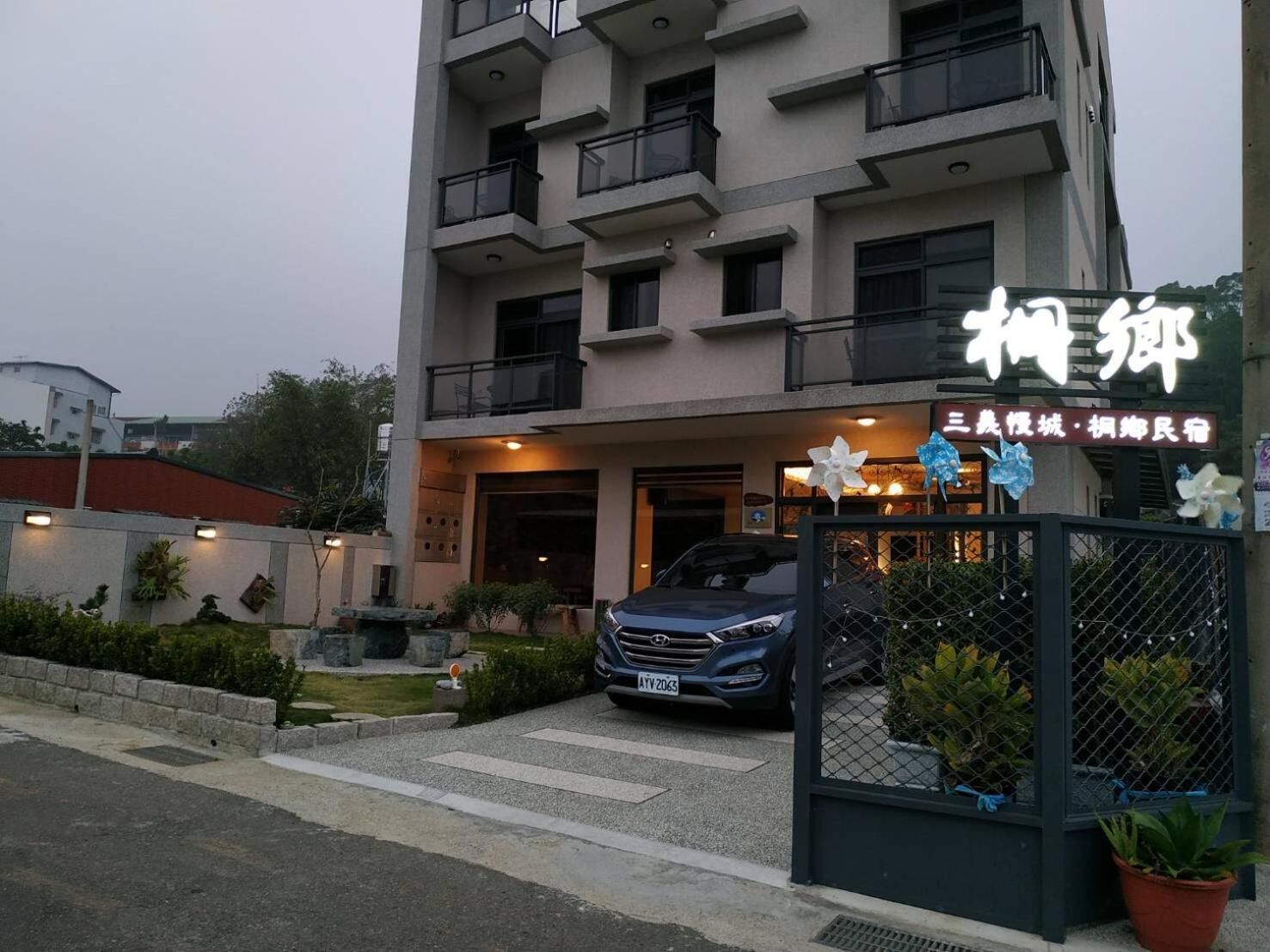 A multi-story building with a gated entrance, a parked car, and potted plants.