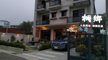 A multi-story building with a gated entrance, a parked car, and potted plants.