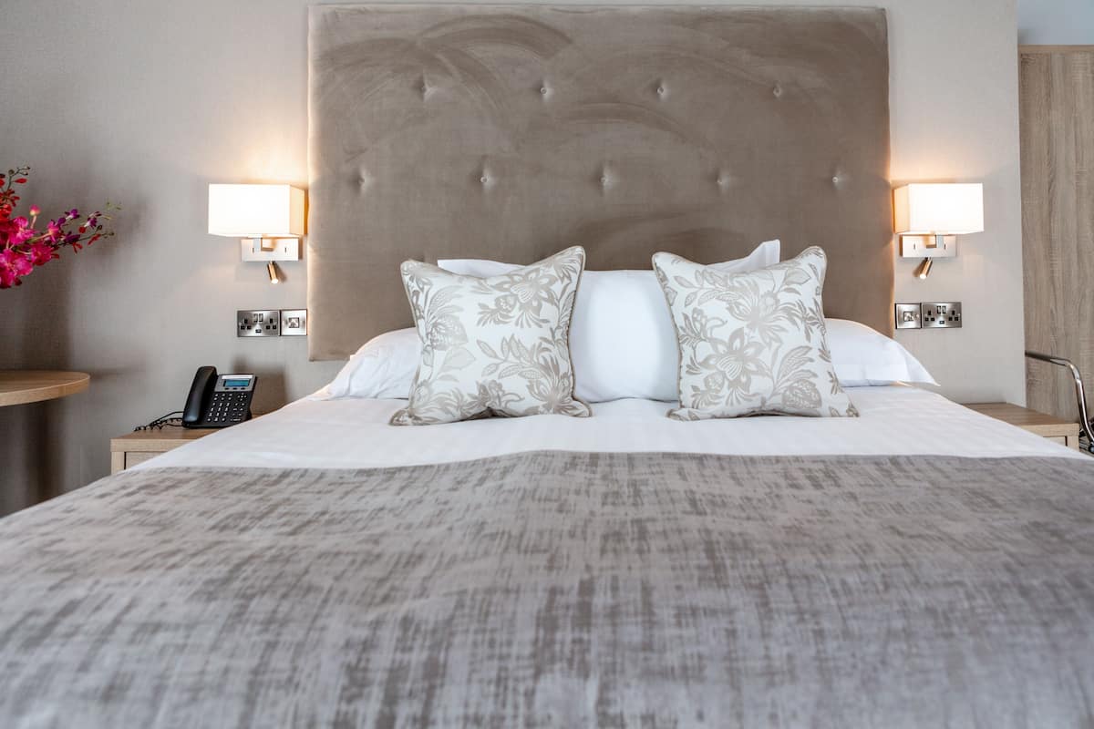 Hotellihuone, jossa on suuri sänky, kaksi yöpöytävalaisinta, puhelin ja yöpöytä, jonka päällä on maljakko täynnä kukkia.