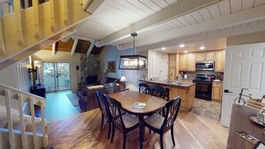 Cozy dining area with a wooden table and chairs, kitchenette, and stone fireplace.