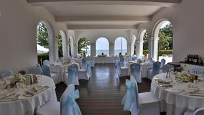 Een balzaal met ronde tafels, ingericht voor een formeel evenement, met witte tafelkleden en blauwe stoellinten.