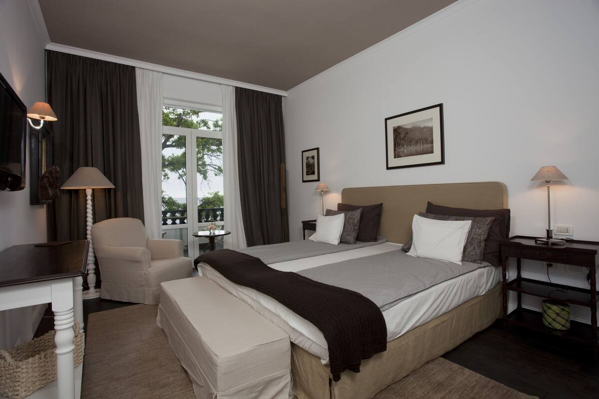 A hotel room with a large bed, two bedside tables, a chair, a desk, and a window with curtains.