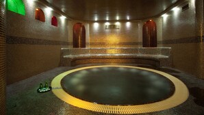 Een wellnessruimte met een rond bubbelbad, een zitgedeelte en betegelde muren.