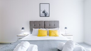A modern hotel room with a large bed, two bedside tables with lamps, a headboard, and a framed picture on the wall. - Hilltop Serviced Apartments - Northern Quarter (Manchester)
