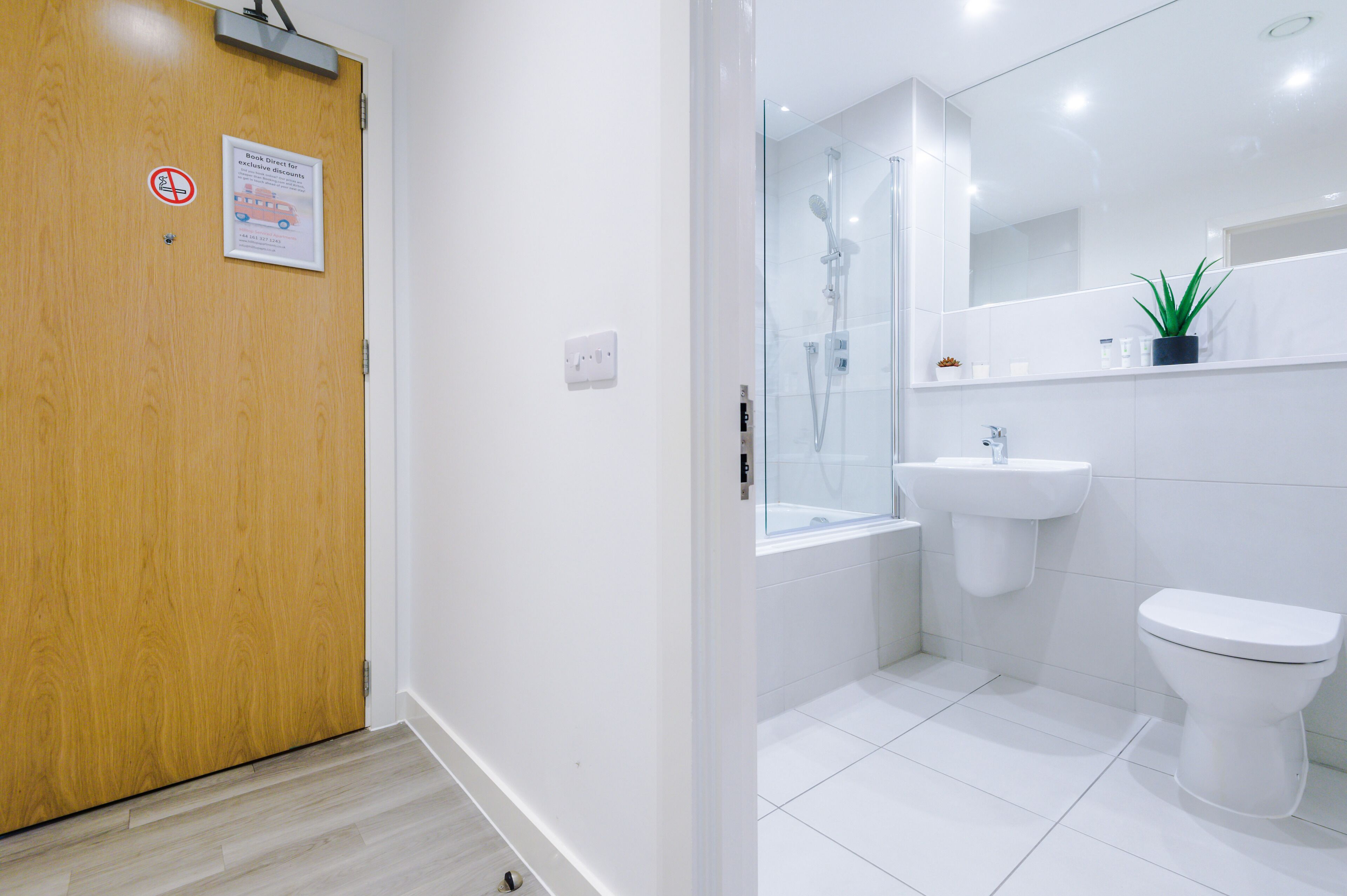 A modern bathroom with a wooden door, a glass shower enclosure, a sink, and a toilet.