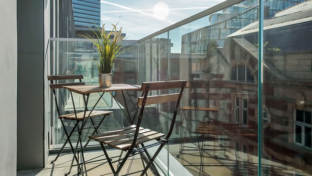 A balcony with a table and chairs, a potted plant, and a view of buildings. - Hilltop Serviced Apartments - Northern Quarter (Manchester)