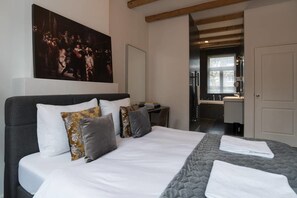 A bedroom with a large bed, a desk, and a bathroom visible through an open door. - Kerkstraat Residence (Amsterdam)
