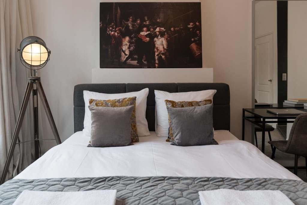 A hotel room with a large bed, two pillows, a desk, a chair, and a floor lamp.