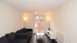 A modern living room with a sofa set, a small white table, and a white cabinet. There is a door with glass panels and a radiator on the wall. - 2 Bedroom Luxury Apartment in Leicester (Leicester)