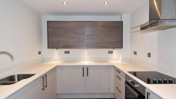 A modern kitchen with a built-in oven, stainless steel sink, and a large wooden panel above the cabinets. - 2 Bedroom Luxury Apartment in Leicester (Leicester)