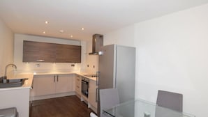 A modern kitchen with white cabinets, a stainless steel refrigerator, and a glass dining table. - 2 Bedroom Luxury Apartment in Leicester (Leicester)