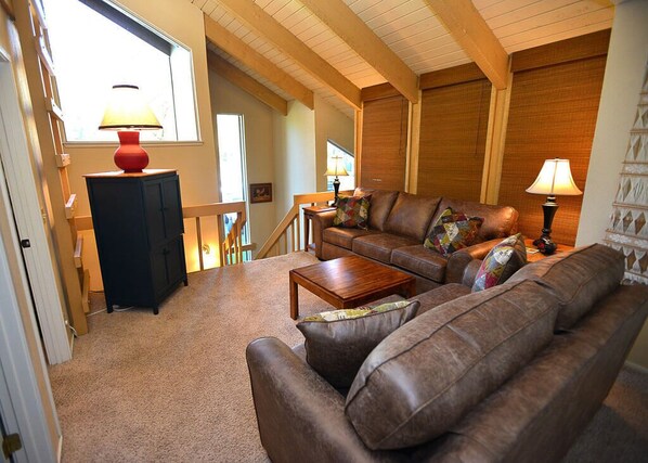 A cozy living room with a brown leather sofa, a wooden coffee table, and a red lamp on a black cabinet. - Sunriver Lodge with Access to The Cove (Sunriver)