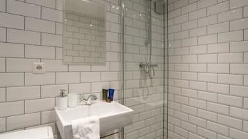 A modern bathroom with white subway tiles, a glass-enclosed shower, a sink with toiletries, and a mirror.