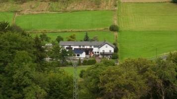 A rural landscape with a house surrounded by green fields and a forested hill.