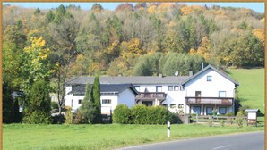 Une maison à deux étages avec un balcon, entourée d’une clôture et de verdure.