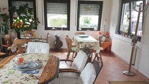 Un coin repas avec une table ronde, des chaises rembourrées et une fenêtre équipée de stores.