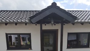 Une maison avec un toit recouvert de tuiles, une porte d’entrée sombre et un petit porche agrémenté d’une lanterne.